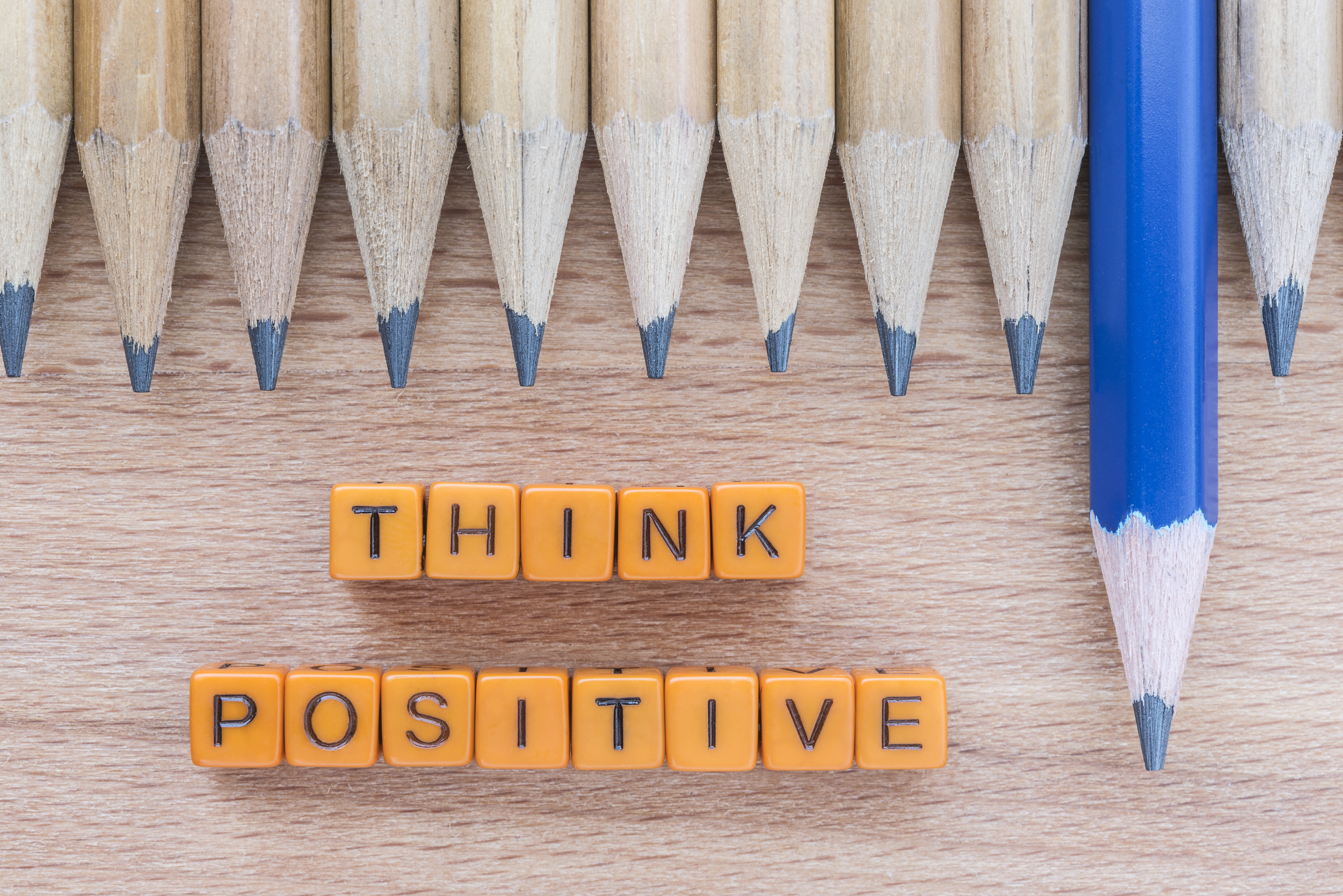 Words Think Positive motivational slogan on wooden table with group of pencils. Top view